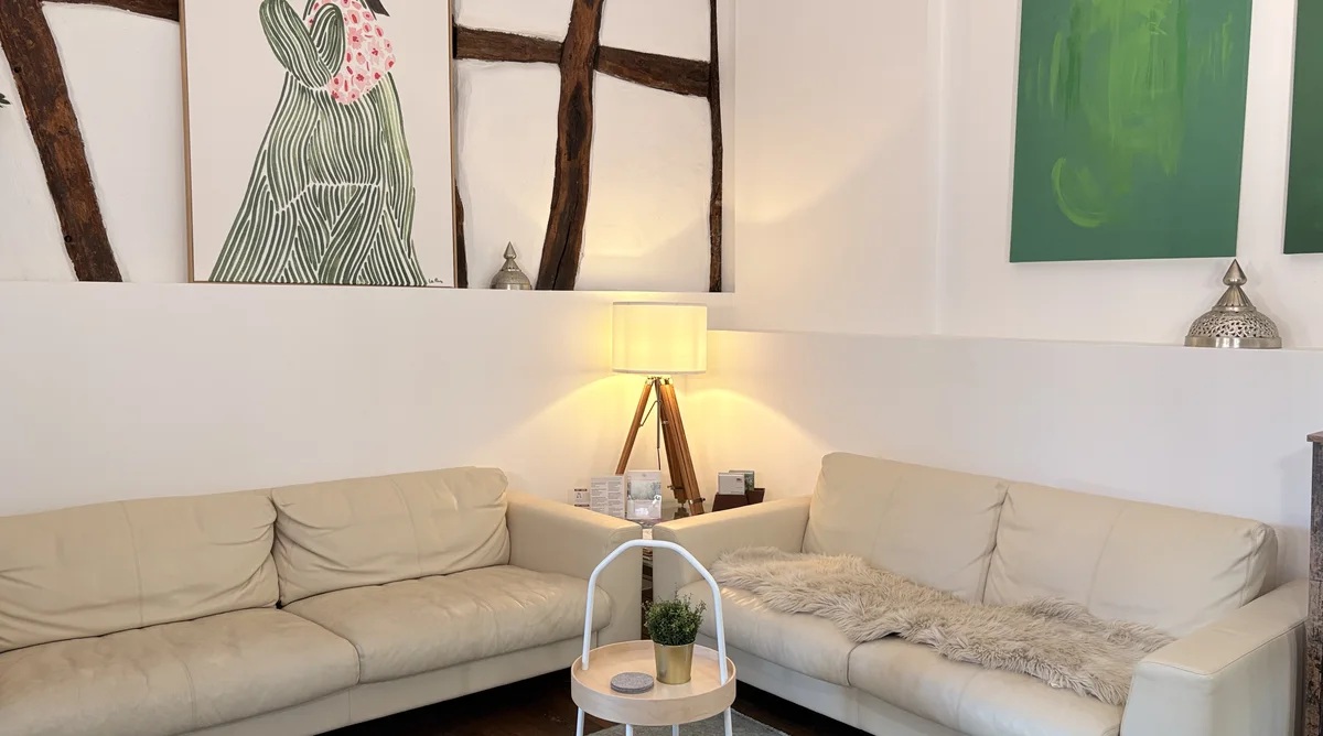 Wartebereich der Naturheilpraxis Deja-Lausmann in Eitorf mit heller Fachwerkwand und bequemen Sofas